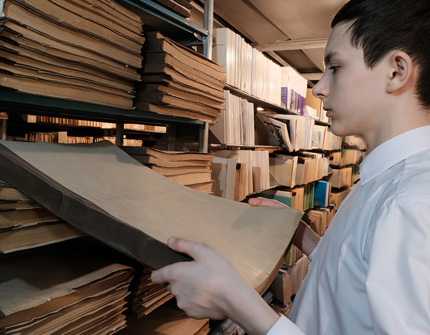 Ein Junge nimmt historische Unterlagen aus einem Regal im Stadtarchiv