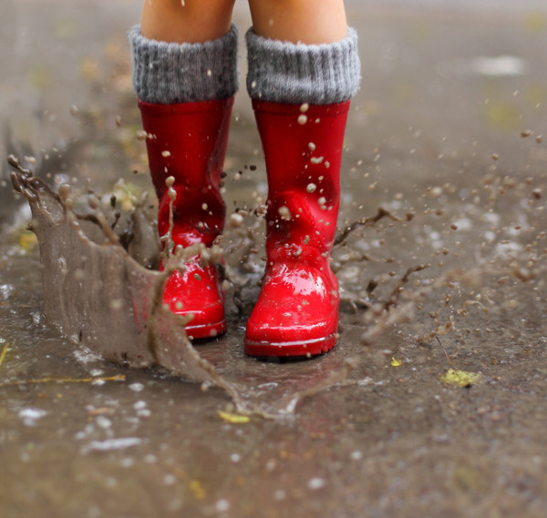 Beine eines Kindes mit roten Gummistiefeln springen in eine Regenpfütze