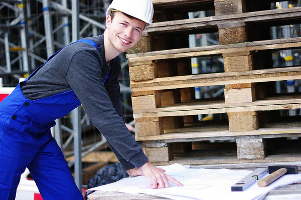 Ein freundlich lächelnder Bauarbeiter zeigt auf einen Plan