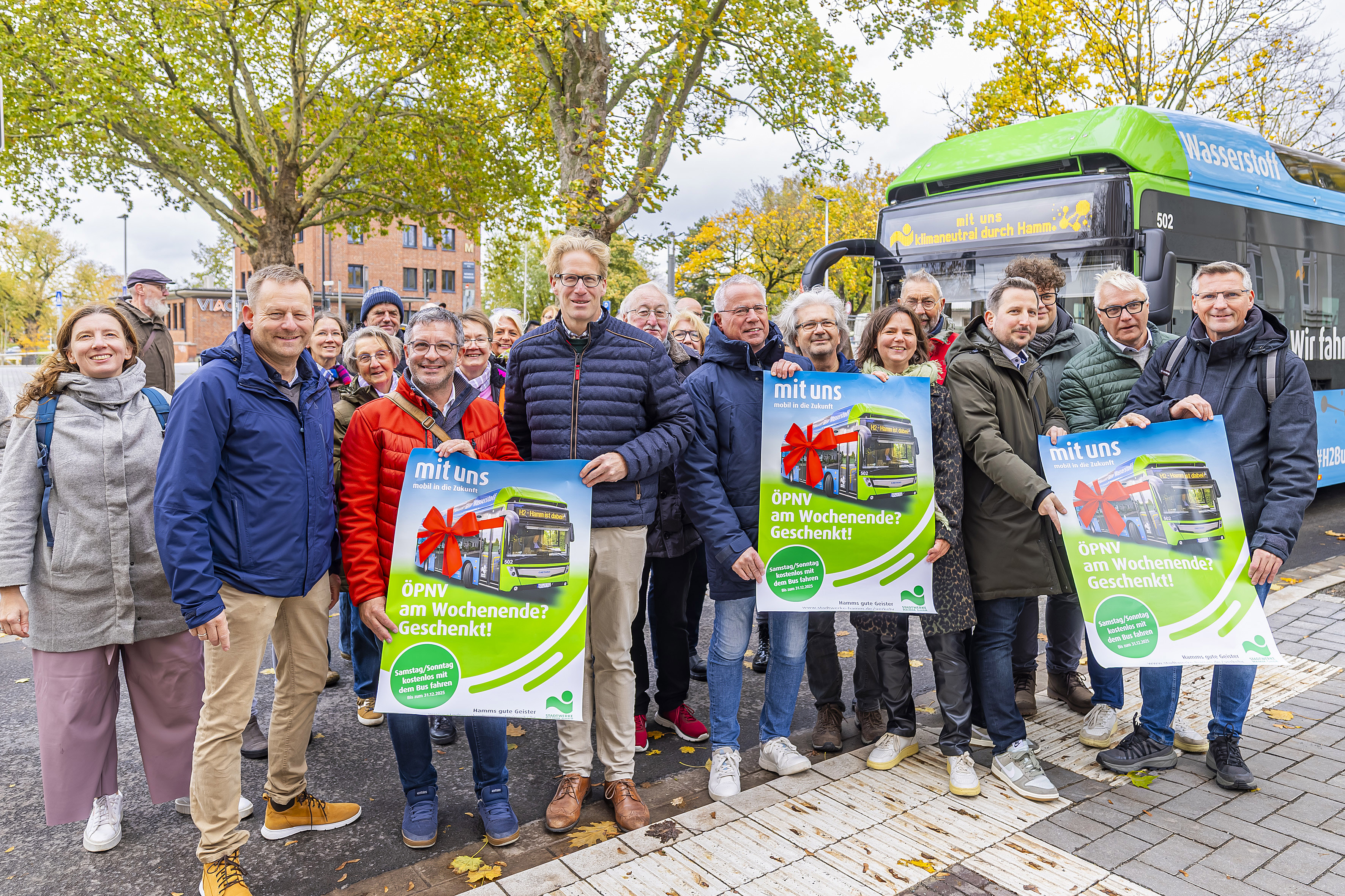 Eine große Gruppe von Personen zeigt vor einem Bus mehrere Plakate