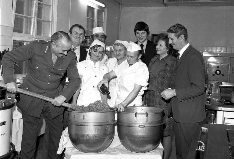 Mehrere Personen stehen in einer K&uuml;che und r&uuml;hren in einem gro&szlig;en Kochtopf im Jahre 1976