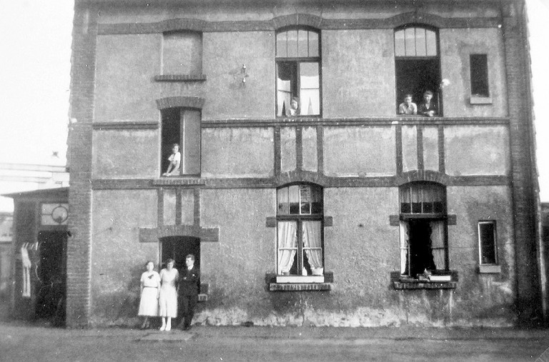 Eine historische Aufnahme eines Wohngeb&auml;udes vor dem zwei Frauen stehen.