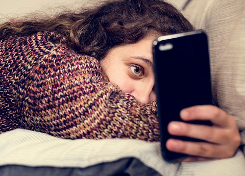 Ein Mädchen liegt auf einem Bett und benutzt ihr Smartphone
