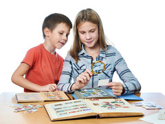 Teenagerin und kleiner Junge betrachten mit Lupe eine Briefmarkensammlung