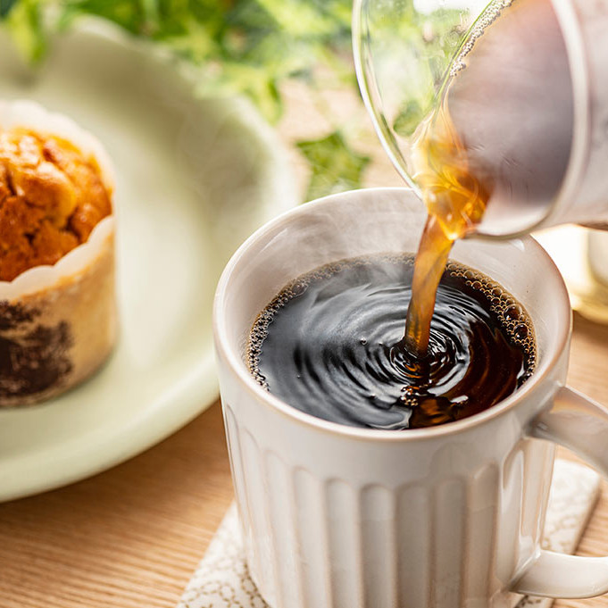 Auf einem Kaffeetisch wird eine Tasse mit Kaffee gef&uuml;llt