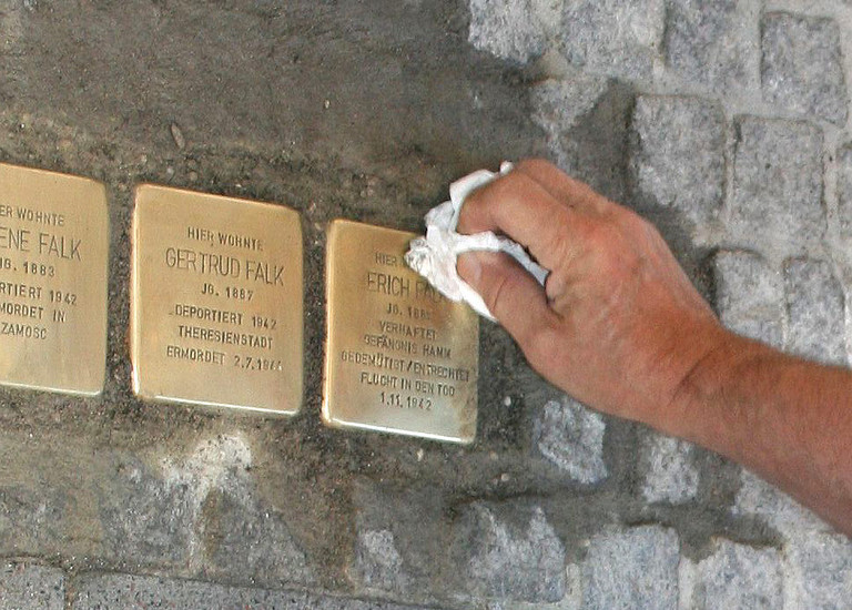 Eine Hand mit einem Lappen putzt gerade verlegte Stolpersteine