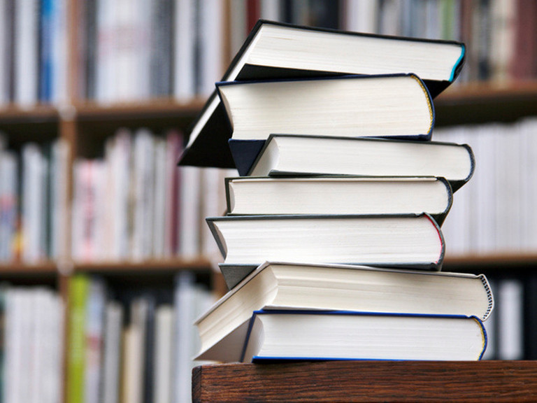 B&uuml;cherstapel mit B&uuml;cherregal im Hintergrund