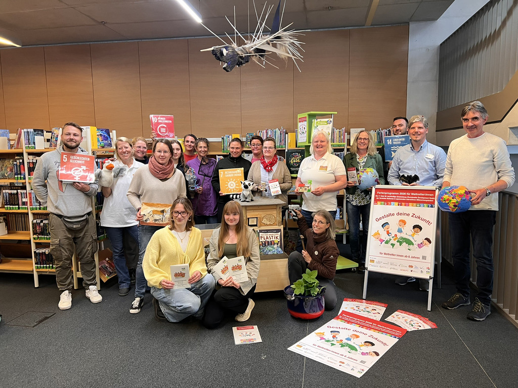 Gruppenfoto von Mitgestaltern des Ferienprogrammes. Die Personen auf dem Bild bewerben das Ferienprogramm mit Plakaten und Broschüren in den Händen.