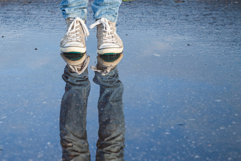 Ein Mensch, der in einer Pfütze steht. Man sieht nur die Füße mit Turnschuhen