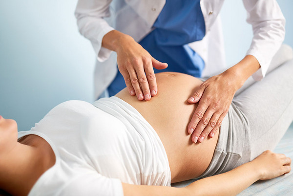 ein Arzt untersucht den Bauch einer schwangeren Frau