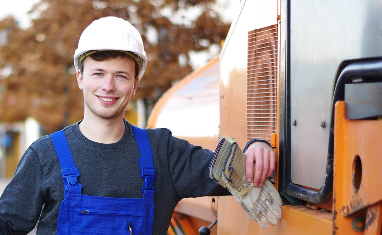 Ein freundlich lächelnder Bauarbeiter steht an einer Baumaschine