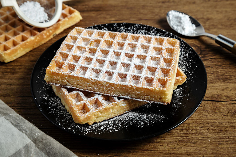 Mit Puderzucker bestreute Waffeln auf einem schwarzen Teller