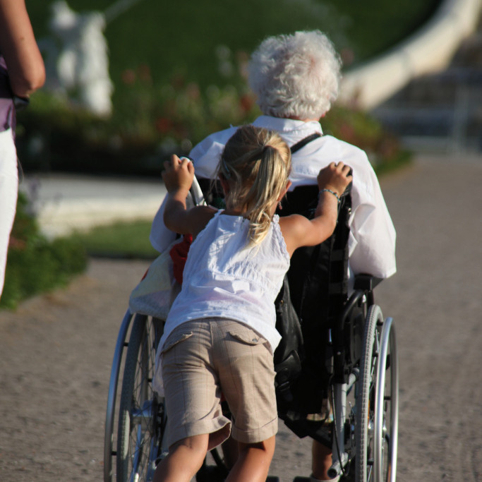 Ein Kind schiebt einen Rollstuhl mit Seniorin