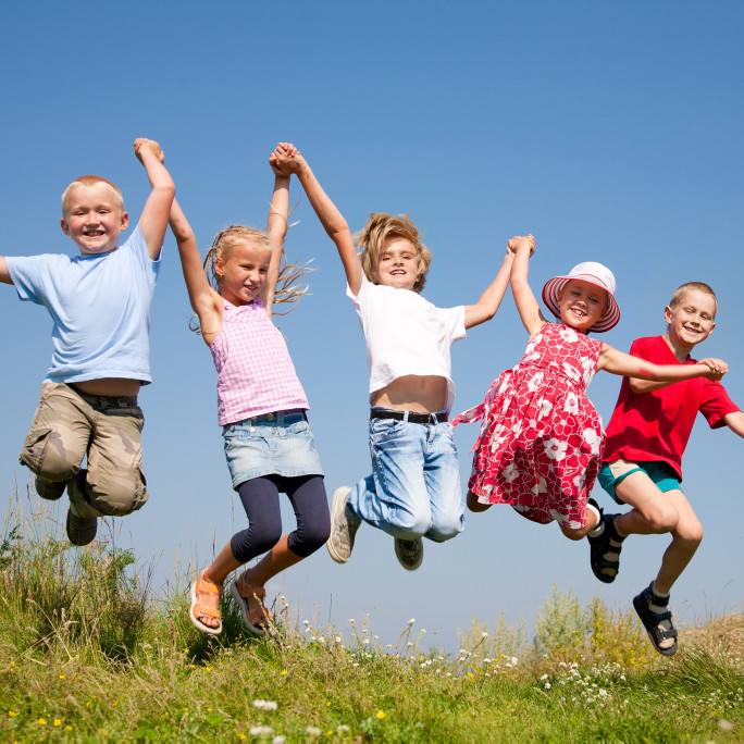 Eine Gruppe fröhlicher Kinder hält sich an den Händen fest und springt in die Höhe