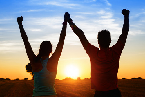 Erfolgreiches junges und athletisches Paar vor einem Sonnenuntergang mit hoch gerissenen Armen nach dem Training