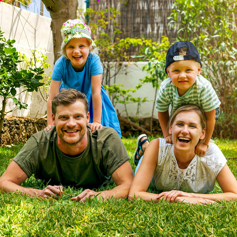 Eine gl&uuml;ckliche Familie mit zwei Kindern, die im Garten hinter dem Haus auf dem Rasen liegt und in die Kamera blickt