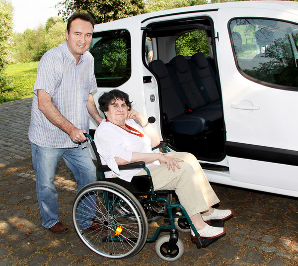 Fotolia 32098253 Ein Mann, der eine Frau im Rollstuhl an ein Auto schiebt
