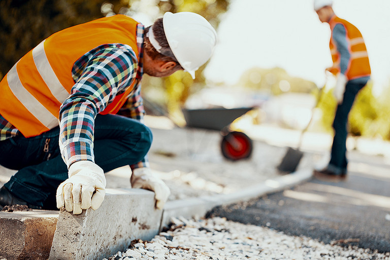 Ein Bauarbeiter verlegt eine Kantenstein auf einer Straßenbaustelle