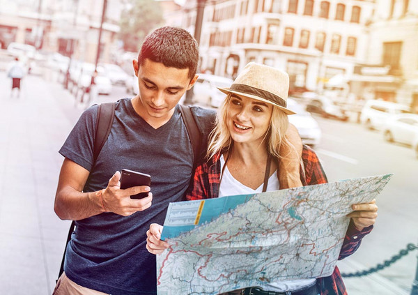 Ein fröhliches Paar geht mit einem Handy und einem Stadtplan durch eine Stadt