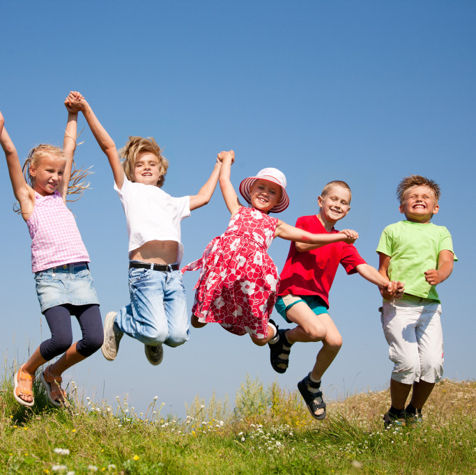Eine Gruppe fröhlicher Kinder hält sich an den Händen fest und springt in die Höhe