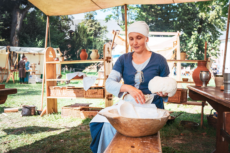 Auf einem mittelalterlichen Markt bereitet eine Frau in einem historischen Gewand einen Brotteig zu.