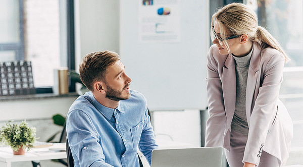 AdobeStock 229543185 Eine junge Frau und ein junger Mann unterhalten sich vor einem Laptop