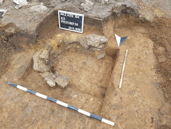 Das Bild zeigt eine Pfostengrube eines ehemaligen vor etwa 800 Jahren errichteten Gebäudes. Gut erkennbar sind die kreisrund angeordneten Verkeilsteine zum stabilisieren des Pfostens.