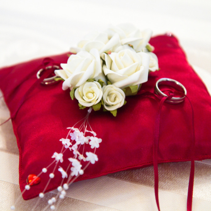 Ein mit weißen Rosen und Trauringen dekoriertes rotes Ringkissen