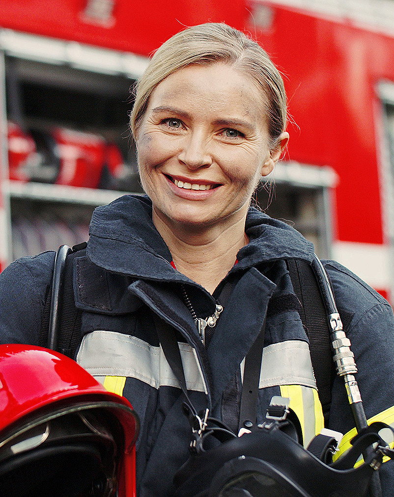 Eine Feuerwehrfrau in Ausrüstung vor einem Feuerwehrwagen