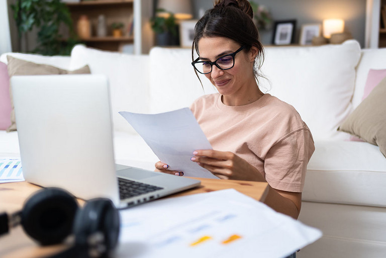 Eine Frau sitzt vor Ihrem Laptop und liest sich ein Schreiben durch