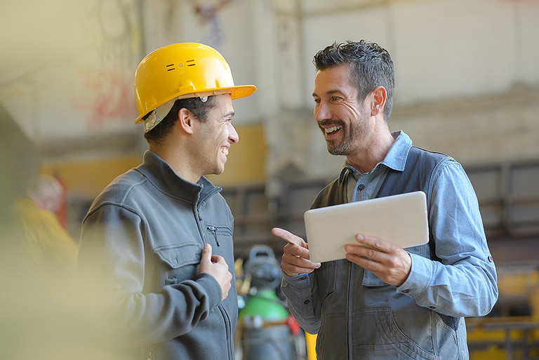 Zwei Arbeiter unterhalten sich lachend in einer Fabrik