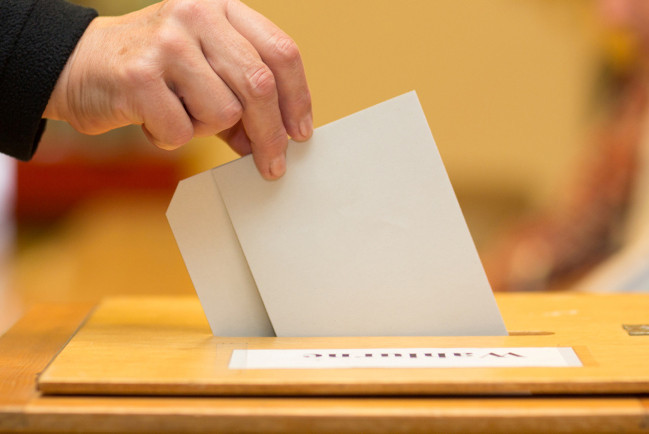 Eine Wahlstimme wird in eine Wahlurne gesteckt 