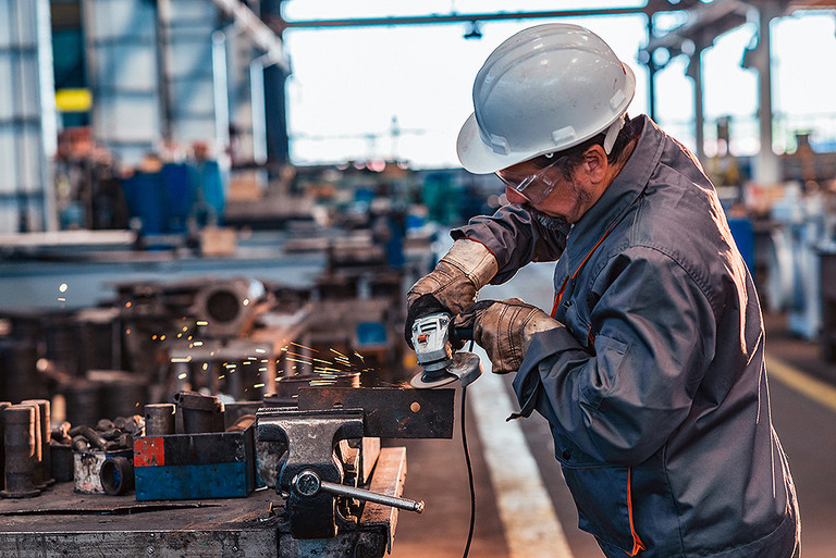 Ein Industriearbeiter bearbeitet ein Stück Metall mit einem Winkelschleifer