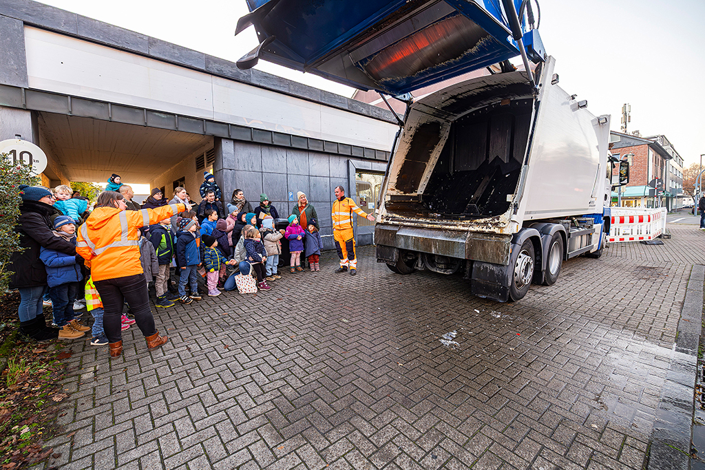 Das Bild zeigt eine Gruppe Kinder, die sich ein Müllauto anschauen. Der Laderaum vom Müllauto ist geöffnet.