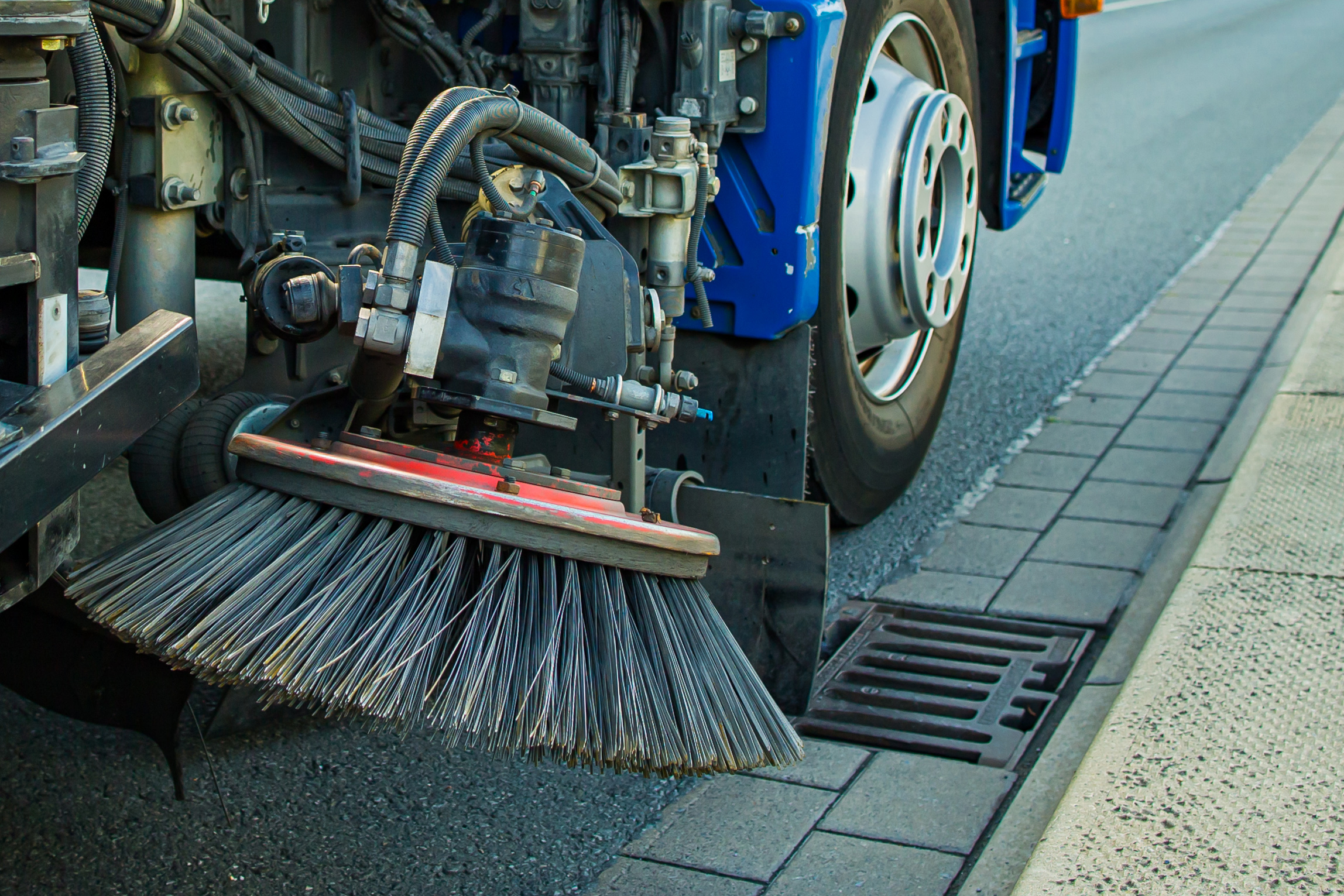 Man sieht den Besen einer Kehrmaschine als Nahaufnahme. Die Kehrmaschine f&auml;hrt auf einer Stra&szlig;e.