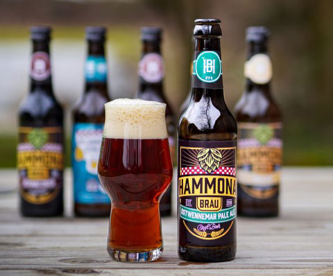 Hammona gefülltes Bierglas mit Hammona-Bräu Flasche daneben, dahinter Bierflaschen unscharf