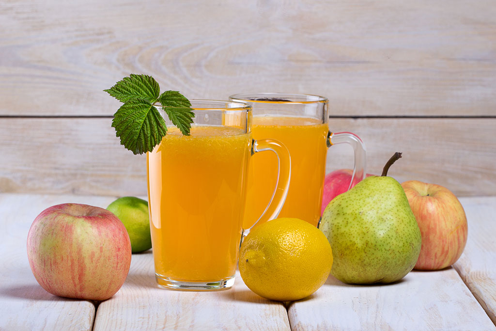 Äpfel, Birne, Zitrone und Fruchtsäfte auf einem Holztisch