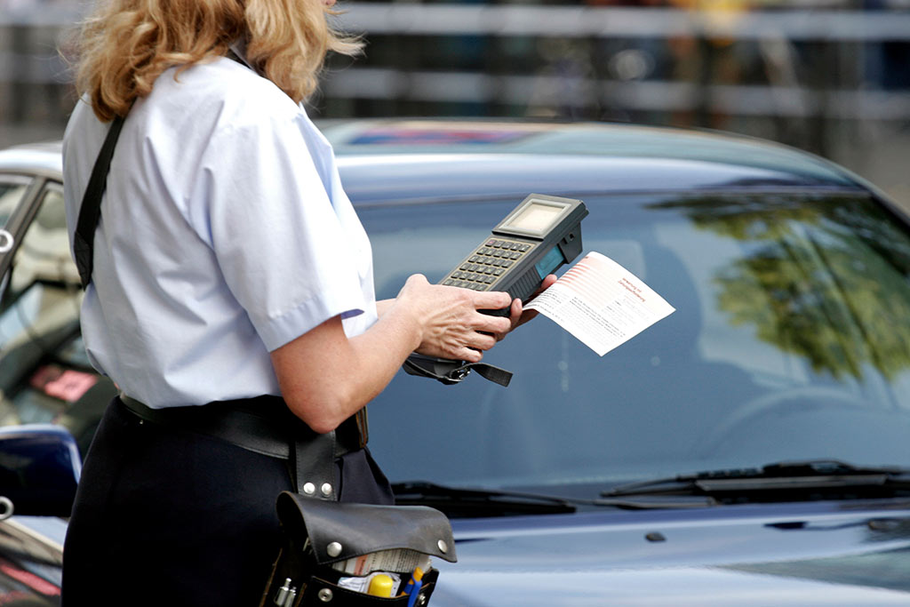 Eine Ordnungsbeamtin verhängt ein Bußgeld an einem parkenden Auto Eine Ordnungsbeamtin verhängt ein Bußgeld an einem parkenden Auto