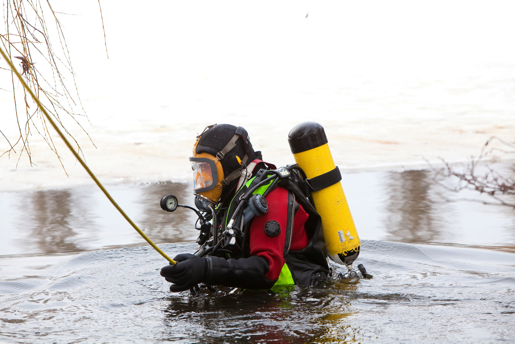 Ein Feuerwehrmann in Tauchausrüstung taucht aus einem zugefrorenen See auf