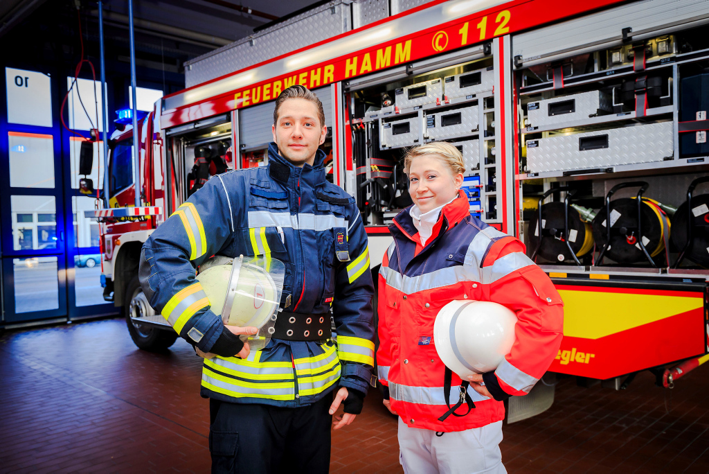 Zwei Mitarbeiter der Feuerwehr Hamm vor einem Feuerwehrwagen