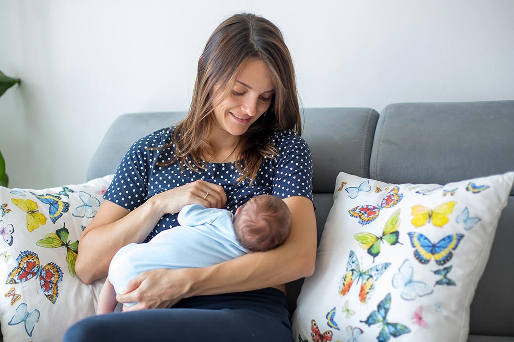 Eine junge Frau stillt ihr Baby auf einem Sofa