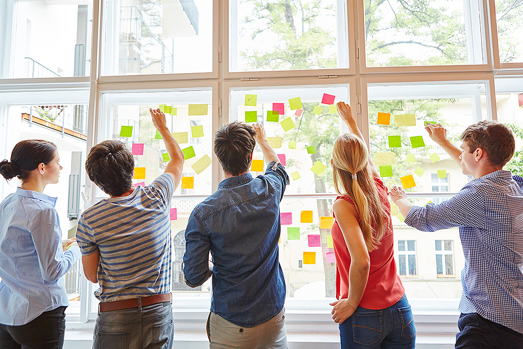 junge Studenten kleben für Brainstorming bunte Zettel an eine Scheibe