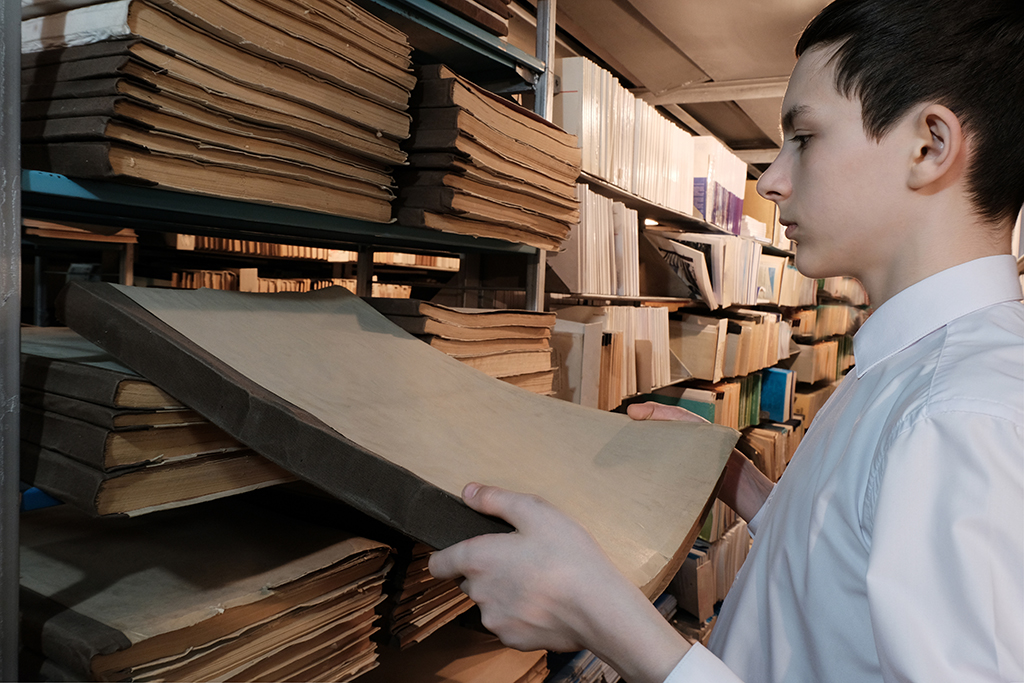 Ein Junge nimmt historische Unterlagen aus einem Regal im Stadtarchiv