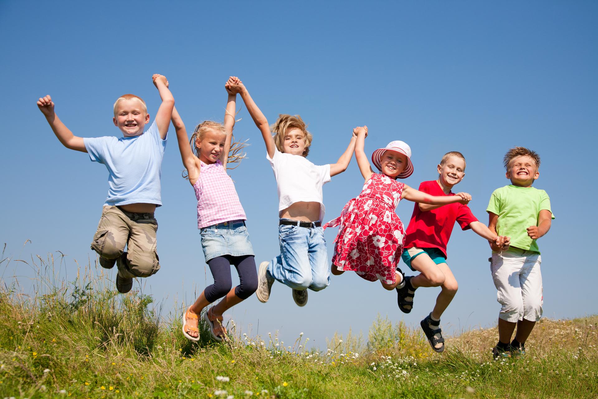 Eine Gruppe fröhlicher Kinder hält sich an den Händen fest und springt in die Höhe 