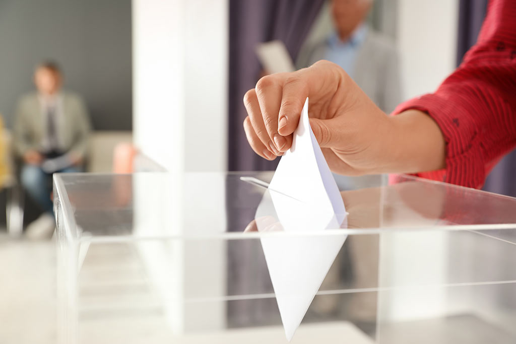 Eine Person steckt eine Wahlzettel in eine Wahlurne