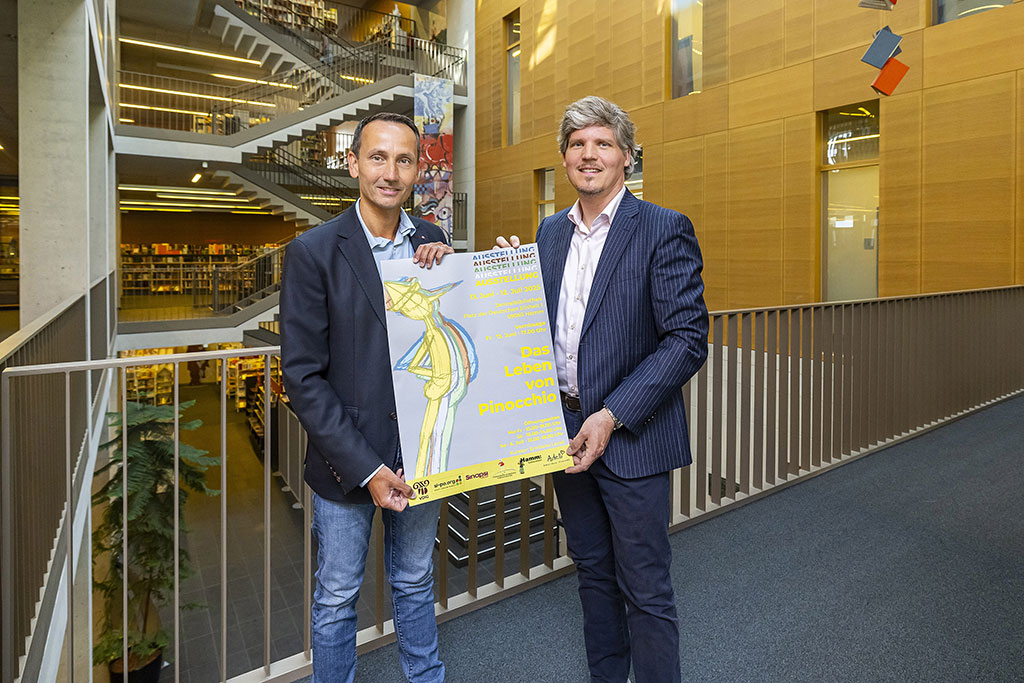 Markus Kreuz und Jens Boyer halten das Plakat zur Pinocchio-Ausstellung