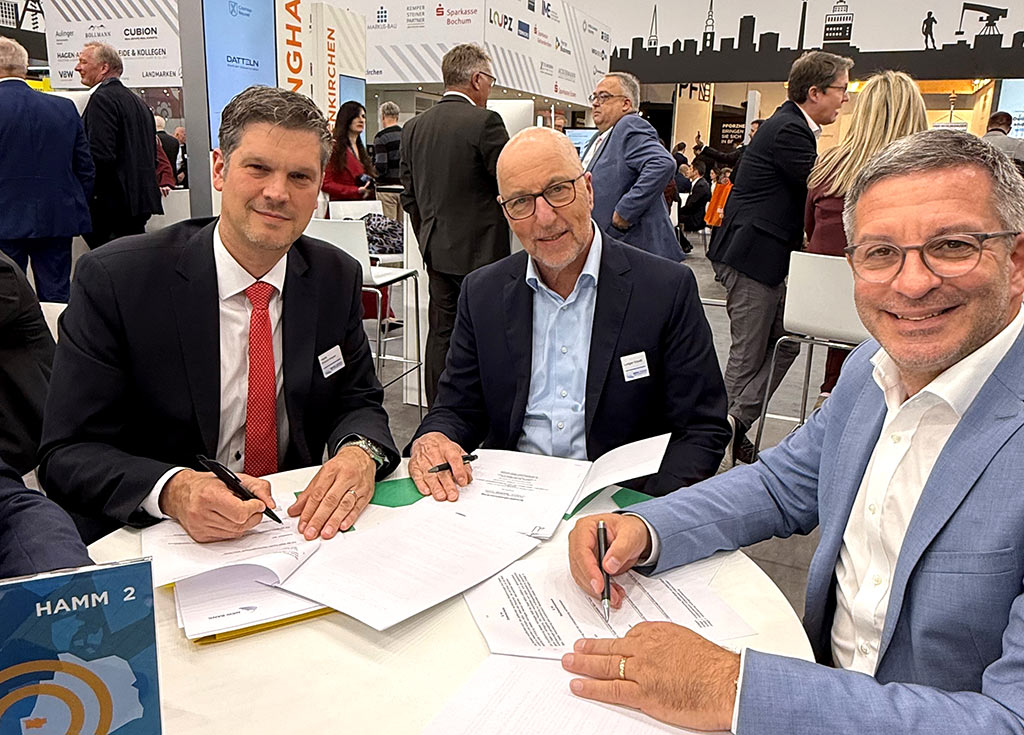 Drei Männer unterzeichnen einen Vertrag auf einer Immobilien-Messe