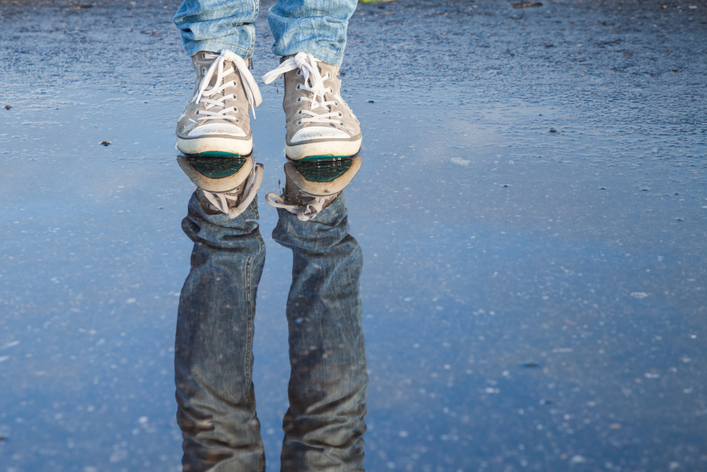 Ein Mensch, der in einer Pfütze steht. Man sieht nur die Füße mit Turnschuhen