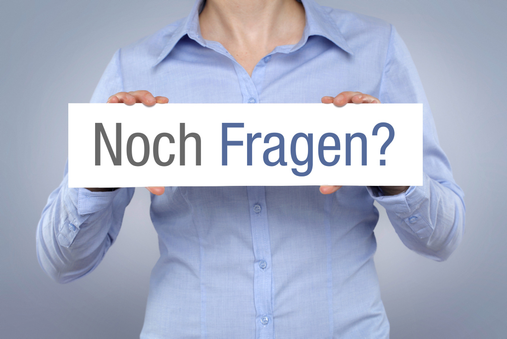 Frau hält Schild in der Hand mit der Aufschrift "Noch Fragen?"