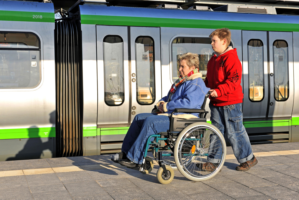 Frau im Rollstuhl auf einem Bahnsteig neben einem Zug